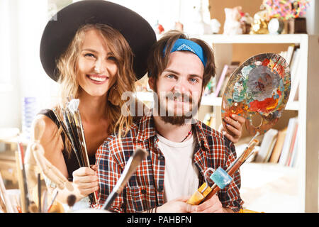 Portrait von fröhlichen Happy weiblich lange Haare artist in süßen schwarzen Hut und bärtige männliche Künstler in Blue bandana mit Pinsel und Palette Stockfoto