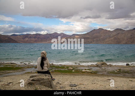 Einsame Frau sitzt auf einem Stein am Rande des Sees und blickt auf den See und Berg.Pangong See in Ladakh, Indien. Kaschmir, Himalaya. Juli 2018. Stockfoto