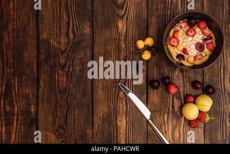 Frühstück mit Haferbrei, Früchten und Beeren auf verwitterte Holz- strukturierte Tabelle auf Hintergrund oder alten Seitenverkleidungen mit Rissen, Kratzern, wirbelt Stockfoto