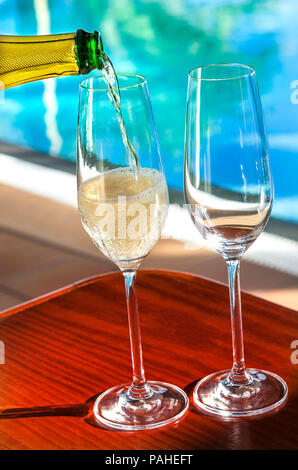 Gießen gekühlte Gläser Champagner Cava auf sonnenbeschienenen Ferienhäuser sonnige Terrasse mit luxuriösen Infinity-Pool im Hintergrund Stockfoto