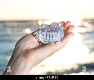 Blau Celestite Cluster aus Madagaskar in die Hand der Frau bei Sonnenaufgang vor dem See. Stockfoto