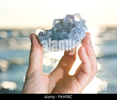 Blau Celestite Cluster aus Madagaskar in die Hand der Frau bei Sonnenaufgang vor dem See. Stockfoto