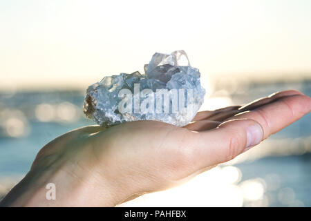 Blau Celestite Cluster aus Madagaskar in die Hand der Frau bei Sonnenaufgang vor dem See. Stockfoto