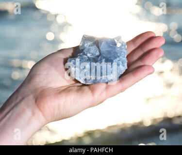 Blau Celestite Cluster aus Madagaskar in die Hand der Frau bei Sonnenaufgang vor dem See. Stockfoto