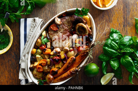 Rindfleisch gebacken mit Gemüse (Kartoffeln, Karotten, Aubergine, Zucchini und Tomate) in Keramik Topf auf Holz- Hintergrund der Ansicht von oben Stockfoto