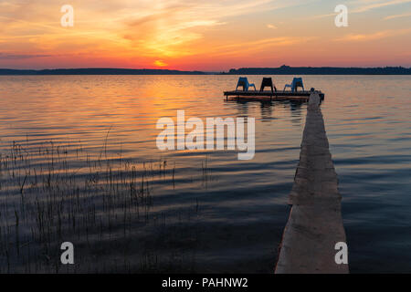 Drei leere Stühle auf hölzernen Steg am See, bei Sonnenaufgang. Stockfoto