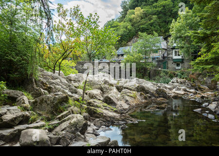 Fluss Llugwy, Betws-y-Coed, North Wales, mit Felsen, grünen Bäumen und Schiefer Gebäude und Brücke im Hintergrund Stockfoto