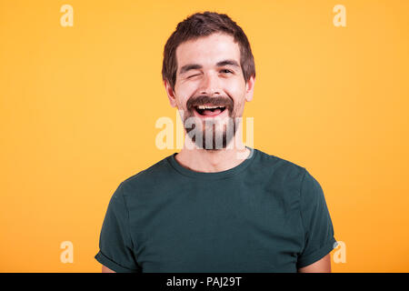 Gerne positiver Mann mit Blick auf die Kamera und zwinkern auf gelbem Hintergrund Stockfoto
