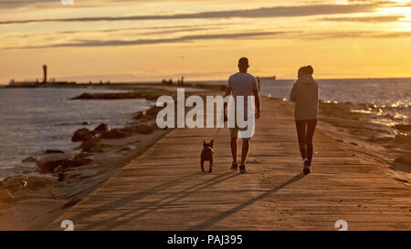 Bei Sonnenuntergang Menschen mit Hund Wandern auf der Mole. Stockfoto