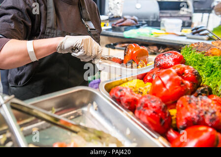 Close up weibliche Verkäufer Hände halten gegrillte Bell peper in Essen zum Mitnehmen. Ein Frühstücksbuffet an einem Feiertag auf der Straße essen kulinarische Markt, fest Stockfoto