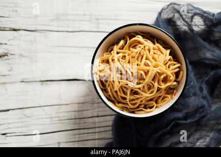 Hohe Betrachtungswinkel und einer weißen Keramik Schüssel mit Yakisoba Nudeln mit Gemüse und Sauce yakisoba, auf einem weißen rustikalen Holztisch mit einige Leere spac Stockfoto