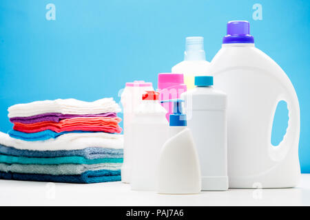 Foto von verschiedenen Flaschen Reinigungsmittel und farbige Handtücher auf Tabelle auf blauem Hintergrund isoliert Stockfoto