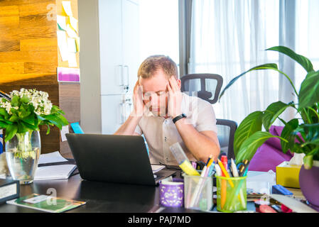 Müde und deprimiert. Frustrierte junge Unternehmer holding Kopf in den Händen, während er auf seinem Arbeitsplatz. Portrait von sorgen junge Busines Stockfoto
