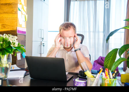 Müde und deprimiert. Frustrierte junge Unternehmer holding Kopf in den Händen, während er auf seinem Arbeitsplatz. Portrait von sorgen junge Busines Stockfoto