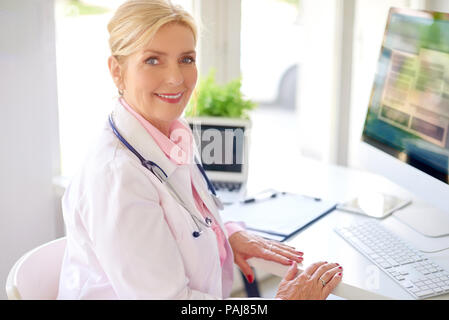 Lächelnd älteren weiblichen Forschung Arzt mit Computer und Laptop, während am Schreibtisch arbeiten. Stockfoto