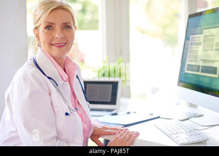 Lächelnd älteren weiblichen Forschung Arzt mit Computer und Laptop, während am Schreibtisch arbeiten. Stockfoto