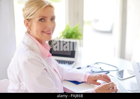 Lächelnd älteren weiblichen Forschung Arzt mit Computer und Laptop, während am Schreibtisch arbeiten. Stockfoto