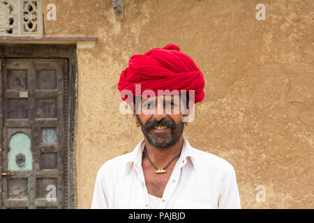 Mann im roten Turban außerhalb einer alten hölzernen Tür in Shahpura, Rajasthan Indien. Stockfoto