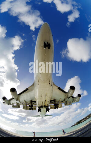 Ein Mann und eine Frau winkt für eine B747 auf Final-Ansatz Landung niedrig über das Meer bei Maho Beach mit ein paar Wolken Stockfoto