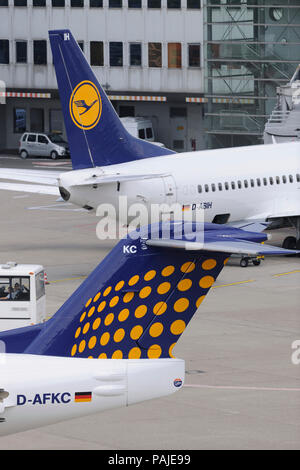 Schwanz-Flossen von Contact Air interregionale Fokker 100 Rollen und Lufthansa Boeing 737 am Terminal hinter geparkt Stockfoto