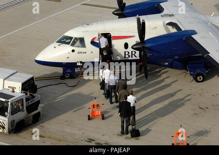 Passagiere mit tragen - auf Beuteln boarding einen British Airways - Sun Air Dornier Do -328-100 am London City geparkt Stockfoto