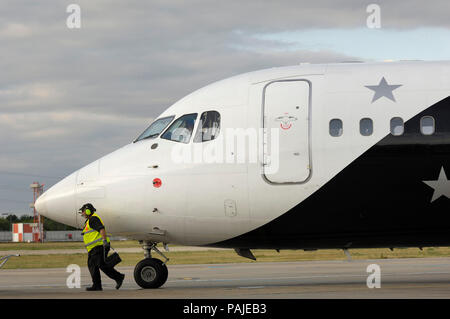 Mann Gelb hohe-viz Waffenrock und Ohr - Verteidiger Keil entfernen aus Bugrad des Titan Airways BAE 146-200 QC am London City geparkt Stockfoto