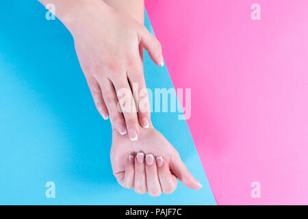 Junge weibliche Hände mit French Maniküre auf die Nägel auf Pastell rosa und blauen Hintergrund isoliert. Weiblichkeit und Schönheit Konzept Stockfoto