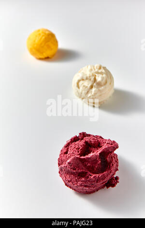 Die drei Kugeln von köstlichen natürlichen Eis - gelbe Mango, Weiße Vanille, roten Beeren auf einem weißen Hintergrund. Soft Focus. Stockfoto