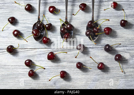 Colorfiul Muster aus drei Löffel mit roten saftigen reifen Kirschen mit Beeren auf einem grauen Hintergrund aus Holz. Stockfoto