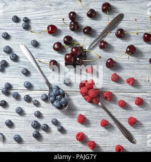 Mischung aus frische organische Beeren Muster von Blaubeeren, Kirschen, Himbeeren auf einem grauen Hintergrund aus Holz. Ansicht von oben. Stockfoto