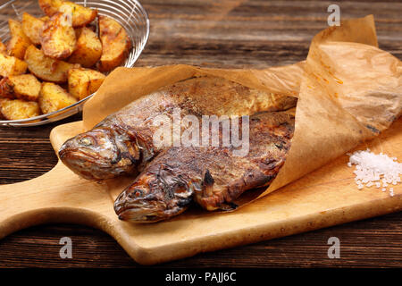 Gegrillter Fisch mit Kartoffeln in Papier eingewickelt auf Holz- Hintergrund Stockfoto