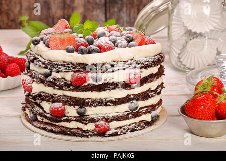 Schokoladenkuchen mit Sahne und frischem Obst auf hölzernen Hintergrund Stockfoto