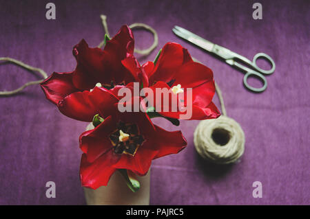 Blumenstrauß nachbearbeiten. Drei rote Tulpen, Garn und Schere. Ansicht von oben Stockfoto