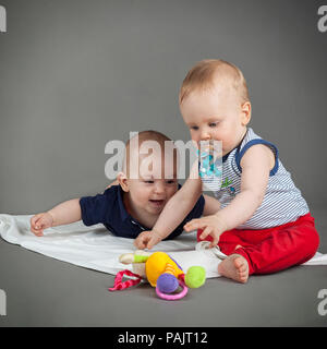Zwei Kleinkind Baby Jungen Kleinkinder Sitzen und Liegen glücklich spielen lächelnd auf grauem Hintergrund. Studio shoot Stockfoto