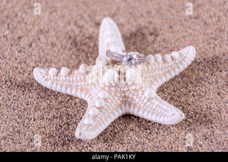 Diamant Verlobung Hochzeit Ring am Seestern auf sandigen Strand, verschwommen und weichen Sand. Schmuck Konzept. Close Up, selektiver Fokus Stockfoto