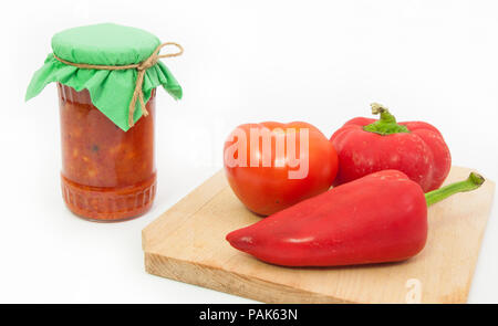 Traditionelle rumänische Gemüse namens zacusca in ein Glas mit frischem Gemüse Konserve auf ein Holzbrett auf weißem Hintergrund isoliert und ein grünes Glas l Stockfoto