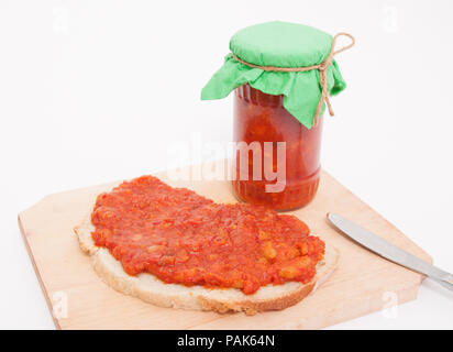 Traditionelle rumänische Gesunde Ernährung Gemüse presevre zacusca genannt in einem Glas und auf einer Scheibe Brot mit einem Messer und ein Schneidebrett verbreiten Stockfoto