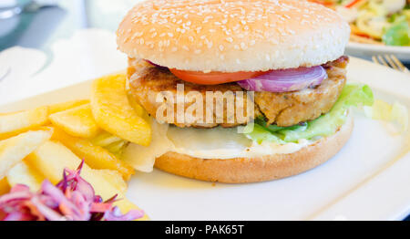 Chicken Burger mit Salat Salat Pommes frites Tomaten Zwiebeln auf eine weisse Platte in einer Ansicht schließen Stockfoto