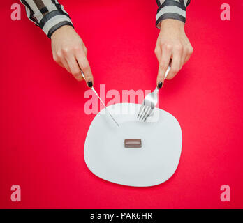 Eine junge Frau auf eine Diät essen ein wenig Schokolade von einem weißen Band schlägt eine strenge Gewichtsverlust Ausgabe Stockfoto