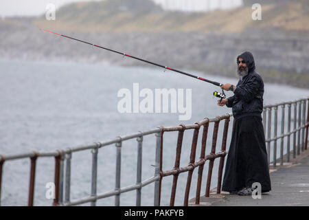 Eine Person, die aussieht wie Jesus Fischen entlang der Promenade von Colwyn Bay im Norden von Wales bei starkem Regen Stockfoto