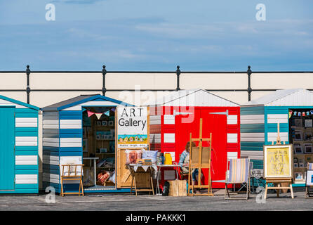 North Berwick, East Lothian, Schottland, Großbritannien, 24. Juli 2018. UK Wetter: Ein Künstler bei der Arbeit in einer der farbenfrohen Strandhütten, die in eine Kunstgalerie im Hafengebiet verwandelt wurden Stockfoto