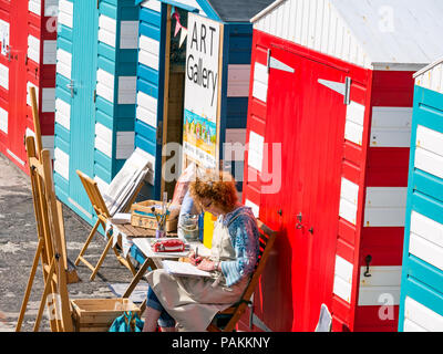 North Berwick, East Lothian, Schottland, Großbritannien, 24. Juli 2018. UK Wetter: Ein Künstler bei der Arbeit in einer der farbenfrohen Strandhütten, die in eine Kunstgalerie im Hafengebiet verwandelt wurden Stockfoto