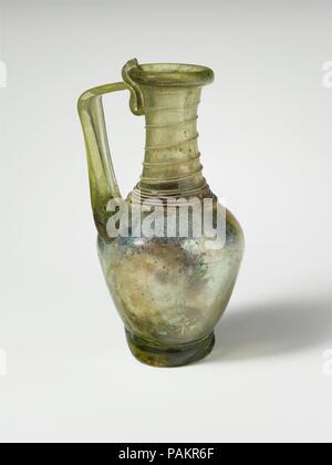 Glaskanne. Kultur: Roman. Abmessungen: H.: 4 3/4 x 2 3/8 x 1 1/4 in. (12,1 x 6 x 3,2 cm). Datum: 4.Jahrhundert N.CHR.. Kleine Kanne. Durchsichtig gelb grün; Griff, ring Fuß, und Trail in der gleichen Farbe. Auch rim gefaltet und im; konkav, zylindrischen Hals, schräge Schulter; Piriform, mit seitlichen verjüngt sich nach unten; dicken Fuß ring, als Spule angewendet; konvexen Boden, mit großen, gezackten pontil Narbe; Strap Griff, mit dicken Rippe auf der einen Seite, angeschlossen an Schulter, erarbeitet und sie sich dann in einem Winkel gedreht, und gefaltet auf die oberen Hals, mit Trail endet am Rand der Felge. Trail von zur Basis Stockfoto