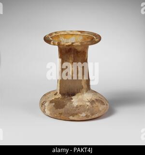 Glas Parfüm Flasche. Kultur: Roman. Abmessungen: Insgesamt: 2 1/2 in. (6,4 cm) Durchm.: 2 3/16 x 1 3/4 in. (5,6 x 4,4 cm). Datum: Ca. 2. nachchristlichen Jahrhundert. Spindel - Typ unguentarium. Farblos mit gelben Farbton. Tubular rim ausgeklappt, über und in und in Breite gedrückt, abfackeln Mund; zylindrische Hals, leicht erweitern nach unten; sehr gedrungenen Körper mit abgerundeten geneigte Seiten; ungleichmäßige unten mit konkaven Zentrum. Intakt; Nadelstich und länglich blasen; Mattierung, Lochfraß, schwache Schillern, und cremig Verwitterung. Museum: Metropolitan Museum of Art, New York, USA. Stockfoto