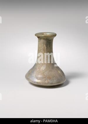 Glas Flasche. Kultur: Roman. Abmessungen: H.: 2 1/2 in. (6,4 cm) Durchm.: 2 x 1 1/16-in. (5,1 x 2,7 cm). Datum: Ca. 2.-3.Jh. N.CHR.. Translucent Hellblau grün. Auch rim, gefaltet und in den Mund; zylindrische Hals, nach unten erweitern und sich unmerklich mit niedrigen konischen Körper mit leicht konvexe Seiten, dann scharf nach innen Kurve zu klein unten mit Kick. Intakt; Blasen und blasen Streifen; Mattierung, leichte Lochfraß, irisieren, und kleine Flecken der Erde Verkrustung und Bewitterung im Außenbereich, dicken Boden Verkrustung, Verwitterung, und brillante Schillern im Innenbereich an. Muse Stockfoto