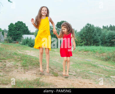 Zwei wunderschöne kleine Mädchen springt auf sonnigen Sommertag. Happy Kids Konzept Stockfoto