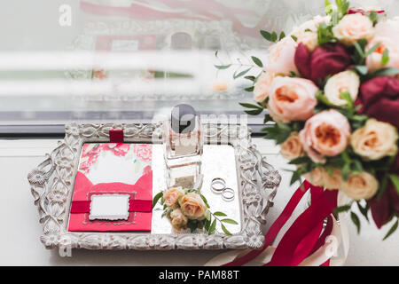 Hochzeit-Blumenstrauß mit Rosen, Pfingstrosen und Seide Bänder, Ringe, Parfüm, Einladungskarten, Anstecker auf silbernem Tablett Stockfoto