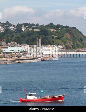 Teignmouth, Devon, England: ein Tourist Boot segelt durch den Fluss Teign Mündung mit Teignmouth Pier und roten Sandsteinfelsen im Hintergrund Stockfoto