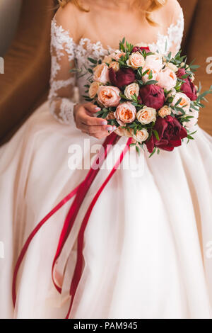 Braut Holding in den Händen schönen Blumenstrauß im klassischen Stil mit Rosen, Pfingstrosen und roten Seidenbändern Stockfoto
