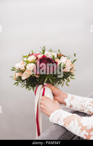 Braut Holding in den Händen schönen Blumenstrauß im klassischen Stil mit Rosen, Pfingstrosen und roten Seidenbändern Stockfoto